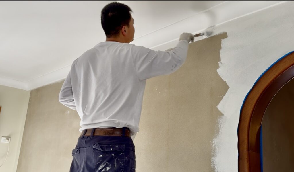 Professional painter applying paint to an internal wall with a brush